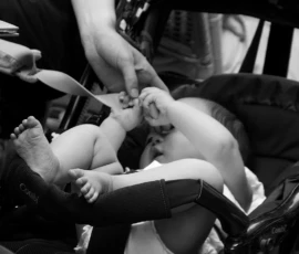 Pascale · 30/05/2026 · 1047 x 1500 Cette photographie en noir et blanc met en scène un **bébé** comme sujet principal, allongé et tenu par une personne dont on voit seulement les mains et les jambes. La **composition** est serrée, centrée sur l'interaction entre le bébé et l'adulte.Le **cadrage** est intimiste, avec des éléments flous en arrière-plan, suggérant un lieu public comme un restaurant. La **lumière** est douce, créant des contrastes subtils. Les **couleurs dominantes** sont les nuances de gris, renforçant une ambiance chaleureuse et nostalgique.Le **style** est documentaire et spontané, évoquant une scène de vie quotidienne. L’**ambiance** est tendre et apaisante, mettant en valeur la vulnérabilité et la connexion humaine.