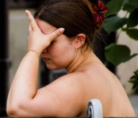 Pascale · 30/05/2026 · 1314 x 1500 Cette photographie met en scène une femme comme sujet principal, les yeux fermés et une main sur le visage, suggérant une posture de fatigue ou de réflexion. Le cadrage est serré, centré sur elle, avec un arrière-plan flou montrant une plante verte et une partie de mur.La lumière semble naturelle et douce, créant des ombres légères. Les couleurs dominantes sont les tons chauds de la peau et les verts de la végétation, avec des touches de rouge dans les cheveux. Le style est réaliste et spontané, évoquant une ambiance intime et mélancolique.