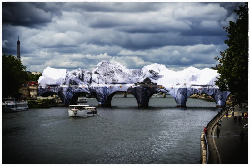 Thierry · 11/06/2026 · 3840 x 2560 Cette photographie met en scène un pont moderne recouvert de structures blanches et géométriques, évoquant des sculptures ou une installation artistique. Le sujet principal est ce pont, dont les formes anguleuses contrastent avec l’eau calme en contrebas.La composition joue sur la symétrie et les lignes droites, renforcée par le cadrage serré sur le pont. La lumière, tamisée par les nuages menaçants, crée une ambiance dramatique. Les couleurs dominantes sont les gris bleutés du ciel et de l’eau, adoucies par les blancs des structures. Le style est photographique, presque cinématographique, avec une touche artistique et une ambiance mystérieuse et légèrement mélancolique.