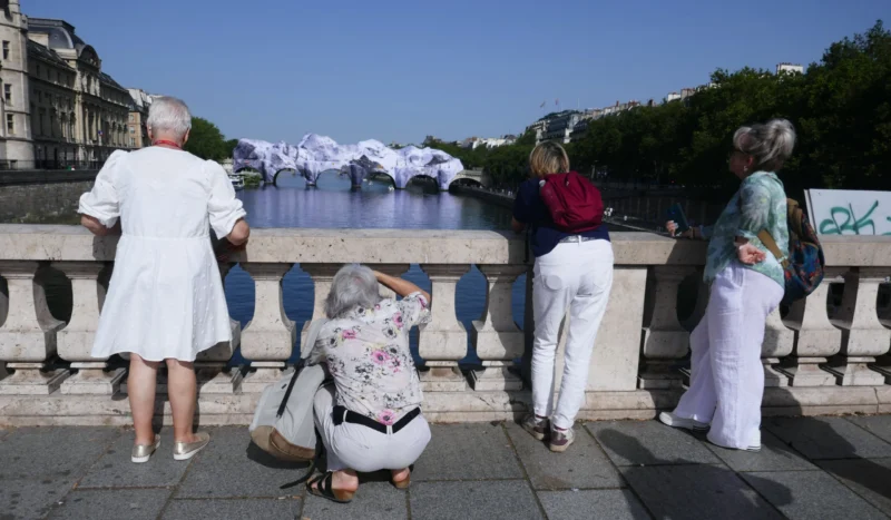 Bao · 5472 x 3193 Cette photographie montre un groupe de quatre personnes âgées sur une promenade en bord de rivière. Le sujet principal est une femme assise au premier plan, les autres debout, observant le paysage.La composition est dynamique, avec un cadrage serré sur les personnages. La lumière est naturelle et éclatante, typique d’un jour ensoleillé. Les couleurs dominantes sont claires et vives : tons pastel des vêtements, bleu du ciel et vert des arbres.Le style est documentaire et réaliste, capturant un moment de vie quotidienne. L’ambiance est paisible et contemplative, renforcée par le cadre apaisant de la nature urbaine.