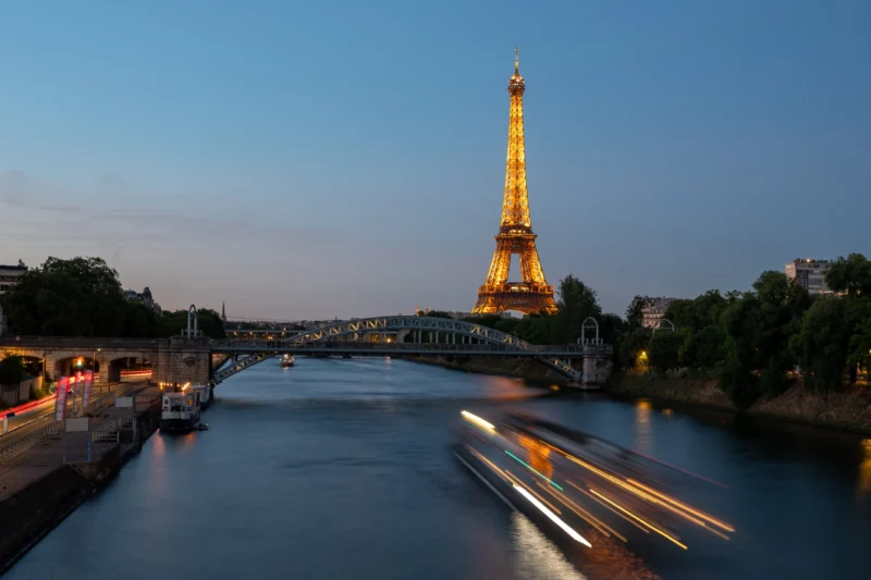 Jean-Marc · 13/06/2026 · 5565 x 3710 Cette photographie met en scène la **Tour Eiffel**, sujet principal, illuminée et dominant le cadre. La composition montre la tour reflétée sur la **Seine**, avec un pont en arrière-plan. Le cadrage est large, capturant aussi des bateaux dont les traînées lumineuses créent un effet dynamique.Les **couleurs dominantes** sont les bleus profonds du crépuscule et les lumières chaudes de la tour. La lumière, douce et tamisée, donne une ambiance **romantique et paisible**, typique d’un style photographique nocturne et artistique.