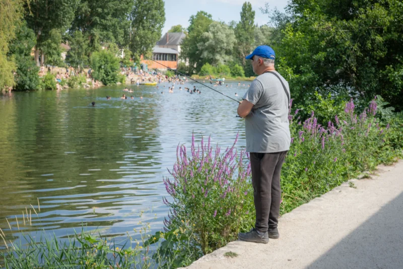 Jean-Marc · 28/06/2026 · 4385 x 2923 Cette photographie montre un homme comme sujet principal, occupé à pêcher au bord d’un plan d’eau calme. La composition est équilibrée, avec l’homme positionné sur la droite, encadré par une végétation luxuriante et des fleurs pourpres en premier plan.Le cadrage est serré, mettant en valeur ses actions et son environnement immédiat. La lumière est naturelle et douce, probablement en journée, créant des ombres légères. Les couleurs dominantes sont les verts de la nature, les bleus du ciel et de l’eau, et les touches de violet des fleurs. Le style est réaliste et documentaire, évoquant une ambiance paisible et sereine.