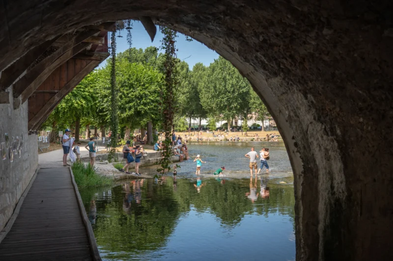 Jean-Marc · 28/06/2026 · 6048 x 4032 Cette photographie capture un **passage voûté** surplombant un plan d’eau. Le **sujet principal** est un groupe de personnes se détendant près de l’eau, sous une arche en pierre.La **composition** joue sur la symétrie et la profondeur, avec l’arche comme élément cadre. Le **cadrage** est serré, mettant en valeur les détails des personnes et des arbres.La **lumière** est naturelle et douce, suggérant un jour ensoleillé. Les **couleurs dominantes** sont les verts des arbres, les tons bleus de l’eau et les gris de la pierre.Le **style** est réaliste et documentaire, évoquant une **ambiance paisible et estivale**.