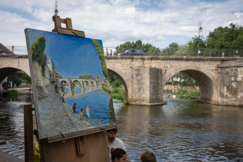 Jean-Marc · 28/06/2026 · 6048 x 4032 Cette photographie montre une toile représentant un pont en pierre sur une rivière, avec des personnages en bas-relief. Le sujet principal est cette peinture, posée sur un chevalet en bois.La composition met en valeur le contraste entre le tableau et le pont réel en arrière-plan. Le cadrage est serré sur l’œuvre, avec une légère inclinaison vers le pont. La lumière est naturelle, douce et légèrement diffuse, créant des ombres douces. Les couleurs dominantes sont les bleus du ciel et de l’eau, les verts des arbres, et les tons gris-beige du pont.L’ambiance est paisible et artistique, évoquant une scène de plein air et de création.