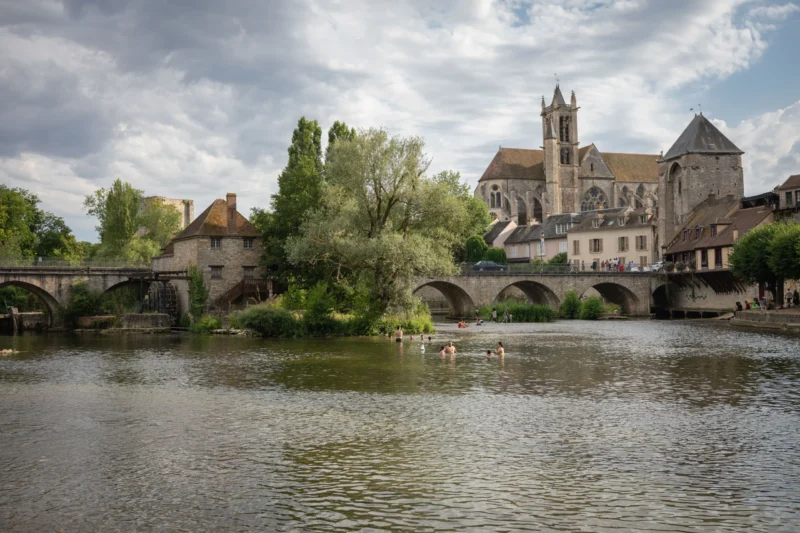 Jean-Marc · 28/06/2026 · 5999 x 3999 Cette photographie met en scène un **pont médiéval** enjambant une rivière, avec en arrière-plan une **église gothique** imposante. La composition est équilibrée, avec le pont au premier plan et l'édifice religieux dominant à gauche.Le cadrage est large, capturant une vue panoramique. La lumière, douce et naturelle, crée des contrastes subtils entre ombres et clartés. Les **couleurs dominantes** sont les verts des arbres, les gris des pierres et les bleus de l’eau.Le style est **réaliste et pittoresque**, évoquant une ambiance **sereine et historique**, typique d’un village européen médiéval.