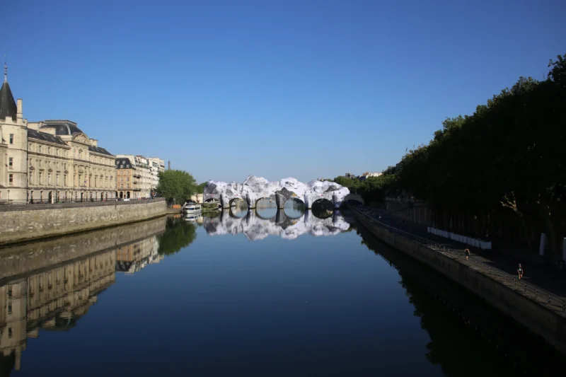 Fabienne · 20/06/2026 · 5472 x 3648 Cette photographie met en scène un pont et un canal reflétant parfaitement les bâtiments environnants. Le **sujet principal** est le pont et son reflet dans l’eau calme, créant une symétrie harmonieuse. La **composition** est équilibrée, avec une ligne horizontale marquée par le miroir d’eau. Le **cadrage** est serré, centré sur le pont et les berges.La **lumière** est naturelle, douce et légèrement latérale, accentuant les contrastes. Les **couleurs dominantes** sont les bleus du ciel et de l’eau, les tons beiges des bâtiments et les verts des arbres. Le **style** est épuré et contemplatif, évoquant une **ambiance** paisible et presque onirique.