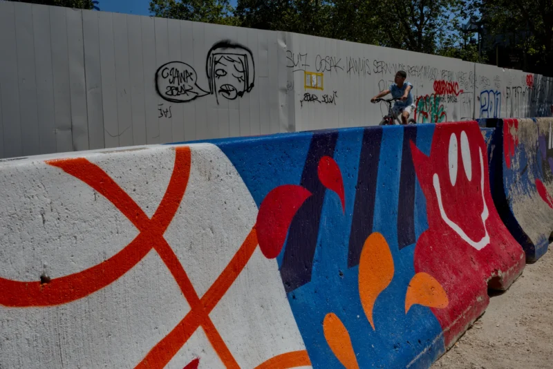 Frédéric · 14/06/2026 · 2517 x 1679 Cette photographie capture un skateur en action devant un mur tagué. Le sujet principal est le skateur en train de réaliser un trick. La composition est dynamique, avec un cadrage serré sur le mur coloré et le skateur en mouvement.Les couleurs dominantes sont vives : bleu, rouge, orange et blanc. La lumière semble naturelle, probablement en journée, éclairant bien la scène. Le style est urbain et énergique, reflétant la culture du street art et du skate. L’ambiance est vibrante et pleine d’action.