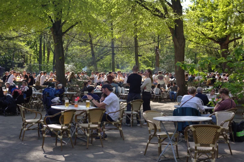 Fabienne · 30/04/2026 · 5175 x 3450 Cette photographie montre un **parc animé** où le **sujet principal** est un **restaurant en plein air**. La composition met en scène de nombreuses tables occupées par des convives, entourées d’arbres.Le **cadrage** est large, capturant une vue d’ensemble. La **lumière** est naturelle et douce, typique d’un jour ensoleillé. Les **couleurs dominantes** sont les verts des arbres et les tons chauds des tables et vêtements.Le style est **documentaire et réaliste**, évoquant une ambiance **détendue et conviviale**, propice aux repas en extérieur.