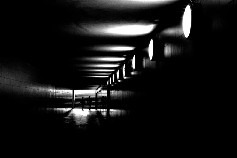 Fabienne · 30/04/2026 · 4257 x 2838 Cette photographie en noir et blanc capture un couloir ou un tunnel long et étroit. Le sujet principal est la perspective linéaire, accentuée par des sources lumineuses alignées créant des jeux d'ombres et de clarté. La composition repose sur des lignes parallèles convergeant vers l'horizon, renforçant la profondeur.Le cadrage serré et la lumière contrastée, avec des halos lumineux, donnent un effet dramatique. Les couleurs dominantes sont les noirs profonds et les blancs lumineux, typiques du monochrome. Le style est épuré et minimaliste, évoquant une ambiance mystérieuse et presque onirique, voire angoissante.