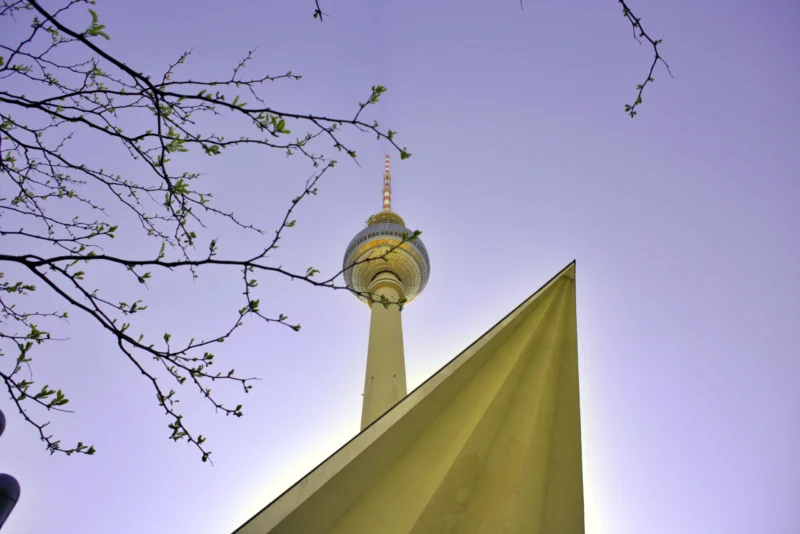 Fabienne · 01/05/2026 · 5496 x 3670 Cette photographie met en scène la **Tour de télévision de Berlin** (Fernsehturm), sujet principal. La composition joue sur le **cadrage serré** et la perspective ascendante, encadrée par des branches d’arbre en premier plan.La lumière douce, probablement crépusculaire, adoucit les contours. Les **couleurs dominantes** sont des tons froids (bleu du ciel) contrastant avec le jaune doré de la structure et les branches nues.Le style est **minimaliste et épuré**, créant une ambiance **sereine et moderne**, mêlant nature et architecture emblématique.