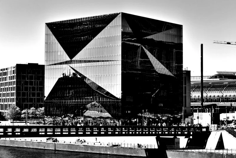 Fabienne · 01/05/2026 · 5496 x 3670 Cette photographie en noir et blanc met en scène un bâtiment moderne aux formes géométriques anguleuses et asymétriques, sujet principal. La composition joue sur les contrastes entre les lignes droites et les angles saillants. Le cadrage inclut une partie du pont et des structures urbaines environnantes, créant une perspective dynamique.La lumière, douce et uniforme, accentue les ombres et les textures architecturales. Les couleurs dominantes, bien que monochromes, exploitent les nuances de gris pour souligner les détails. Le style architectural est contemporain et avant-gardiste, évoquant une ambiance à la fois futuriste et urbaine.