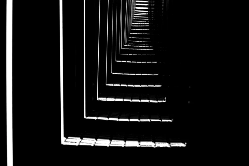 Fabienne · 01/05/2026 · 5496 x 3670 Cette photographie montre une perspective trompeuse de lignes parallèles qui semblent converger vers un point, créant un effet de tunnel. Le sujet principal est cette illusion d’optique géométrique.La composition repose sur un cadrage serré et une symétrie parfaite. La lumière, douce et uniforme, met en valeur les contours nets des lignes blanches sur fond noir. Les couleurs dominantes sont le blanc et le noir, renforçant le contraste.Le style est épuré et minimaliste, évoquant une ambiance mystérieuse et hypnotique, presque abstraite.