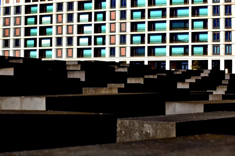 Fabienne · 01/05/2026 · 5496 x 3670 Cette photographie met en scène un **mur de béton brut** en premier plan, composé de blocs irréguliers. En arrière-plan, une **façade de bâtiment** aux fenêtres colorées et multicolores, reflétant des teintes vives (bleu, rouge, vert).Le **cadrage** est serré, créant un contraste entre les formes géométriques rigides et les couleurs dynamiques. La **lumière** semble naturelle, avec des ombres marquées, renforçant le côté dramatique. Les **couleurs dominantes** sont froides et minérales en avant, opposées aux tons chauds et éclatants derrière.Le style évoque une **ambiance urbaine et moderne**, mêlant brutalité et poésie.