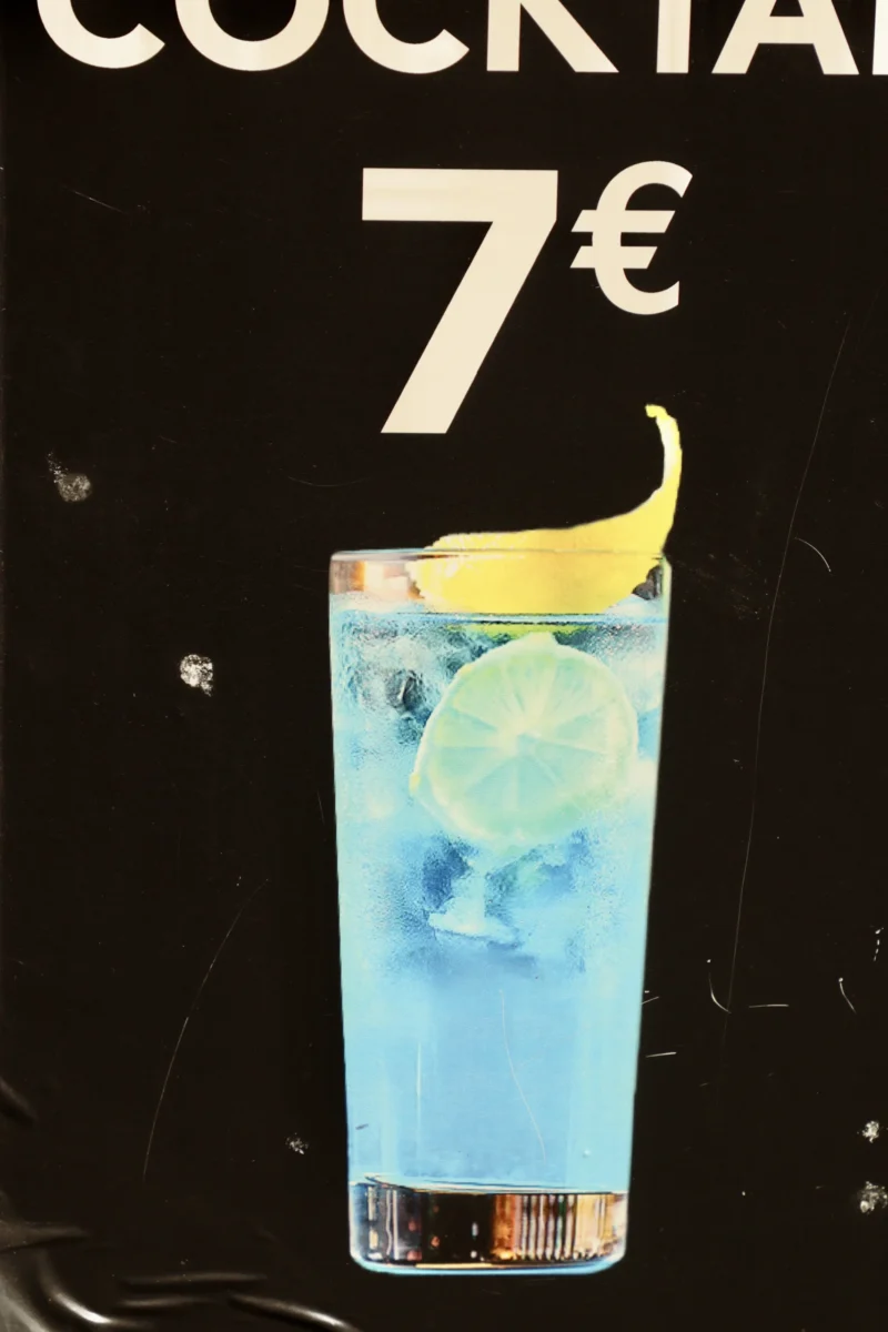 Francoise · 20/06/2026 · 4000 x 6000 Cette photographie montre un cocktail comme sujet principal. Le cadrage est serré sur un verre transparent rempli d’une boisson bleue, garnie d’une tranche de citron vert et d’une rondelle de citron flottante. La composition est épurée, avec un fond noir mettant en valeur le verre.Les couleurs dominantes sont le bleu électrique du cocktail et le jaune vif du citron. La lumière semble artificielle, dirigée pour accentuer les détails et créer un contraste marqué. Le style est publicitaire, évoquant une ambiance moderne et attrayante, typique d’un bar ou d’une enseigne de restauration.