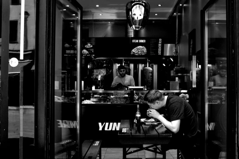 Fabienne · 02/05/2026 · 4459 x 2973 Cette photographie en noir et blanc montre deux personnes travaillant dans un espace confiné, probablement un laboratoire ou un atelier de mixage audio.Le sujet principal semble être l’un des individus, penché sur son travail. La composition est symétrique avec des éléments structurés comme des étagères et des équipements. Le cadrage est serré, mettant en valeur les détails techniques.La lumière est tamisée, créant des contrastes marqués. Les couleurs dominantes, en monochrome, accentuent les textures et les ombres.Le style est documentaire et industriel, évoquant une ambiance concentrée et professionnelle.