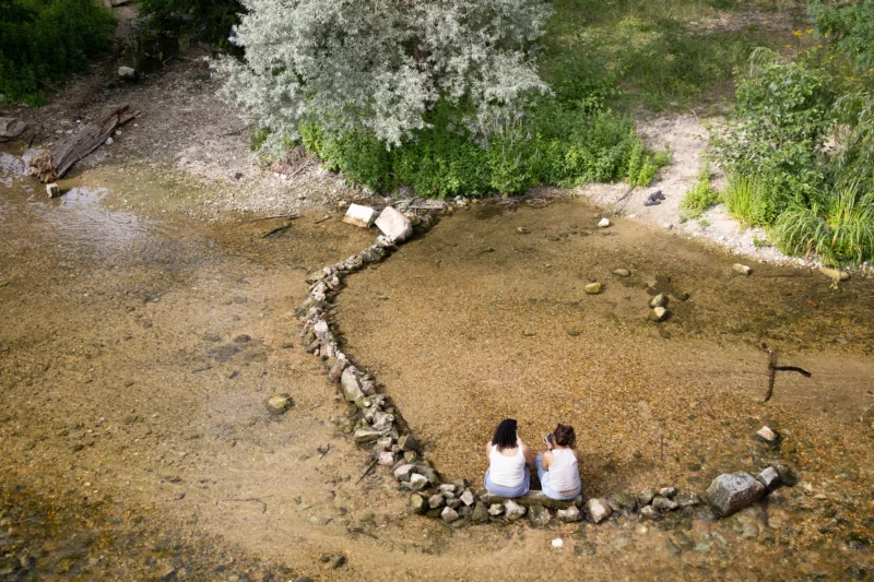 Muriel · 28/06/2026 · 2048 x 1365 Cette photographie montre deux enfants assis sur un chemin de pierres dans un cadre naturel. Le sujet principal est leur silhouette, encadrée par un sentier sinueux bordé de cailloux.La composition est aérée, avec une perspective aérienne. Le cadrage met en valeur le contraste entre les enfants et l’environnement minéral et végétal. La lumière semble douce et naturelle, probablement en journée.Les couleurs dominantes sont les tons terreux (beige, brun) et verts, créant une ambiance paisible et sereine. Le style est documentaire et poétique, évoquant la simplicité et la connexion avec la nature.