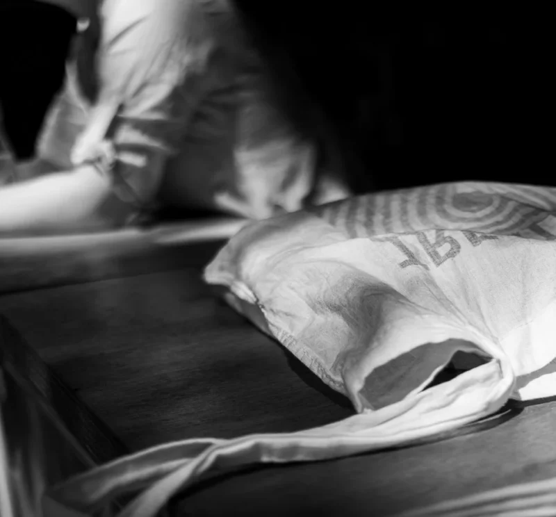 Laurence · 14/06/2026 · 968 x 900 Cette photographie en noir et blanc met en scène un objet partiellement enveloppé dans un tissu, probablement un vêtement ou un accessoire. Le sujet principal semble être une main ou un bras tenant un objet, partiellement hors-champ.La composition est simple et épurée, avec un cadrage serré qui isole les éléments. La lumière est douce et tamisée, créant des contrastes subtils et des ombres marquées. Les tons dominants sont les gris et noirs, renforçant une ambiance mystérieuse et intime. Le style est minimaliste et artistique, évoquant une atmosphère contemplative et presque onirique.