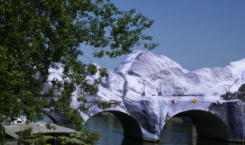 Bao · 5358 x 3183 Cette photographie met en scène un **pont enjambant une vallée montagneuse**. Le **sujet principal** est la chaîne enneigée imposante en arrière-plan, partiellement cachée par des **arbres feuillus** en premier plan.La **composition** joue sur le contraste entre la nature verdoyante et les sommets blancs. Le **cadrage** est serré sur le pont et les montagnes, créant une perspective profonde. La **lumière** est naturelle et vive, suggérant un jour ensoleillé. Les **couleurs dominantes** sont les verts des feuilles, les blancs de la neige et les gris du pont.Le **style** est réaliste et photographique, évoquant une **ambiance paisible et majestueuse**, mêlant sérénité et grandeur naturelle.