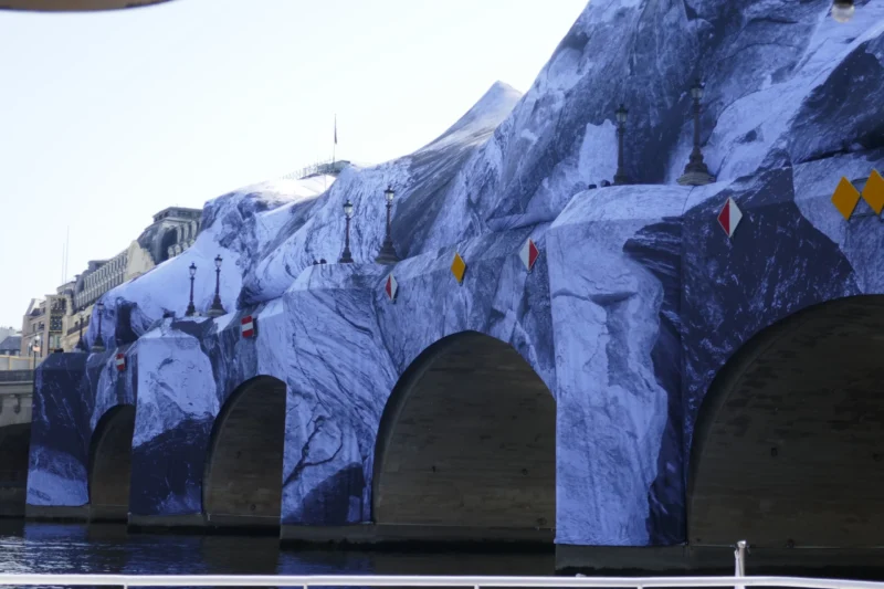 Bao · 5472 x 3648 Cette photographie montre une structure architecturale stylisée évoquant une montagne rocheuse et glacée. Le sujet principal est une façade décorative aux arches sombres, imitant des grottes ou des tunnels.La composition est horizontale, avec un cadrage serré sur les arches et une partie du ciel visible en haut. La lumière est naturelle, douce, mais contrastée, créant des ombres marquées. Les couleurs dominantes sont les bleus glacés et les gris, renforçant l’ambiance froide et minérale.Le style semble inspirée par un univers fantastique ou cinématographique, évoquant une ambiance mystérieuse et immersive.
