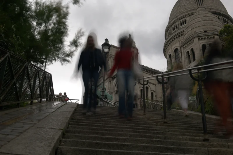 Bao · 6024 x 4016 Cette photographie montre deux personnes en mouvement sur un escalier extérieur, légèrement floues, suggérant un effet de vitesse. Le sujet principal est l’architecture imposante en arrière-plan, un bâtiment avec une coupole et des colonnes, évoquant un style classique.Le cadrage est dynamique, avec une composition en contre-plongée. La lumière est tamisée, créant une ambiance sobre et légèrement dramatique. Les couleurs dominantes sont les tons gris et beiges, adoucis par des touches de rouge et de vert. L’ensemble dégage une atmosphère à la fois urbaine et contemplative, mêlant mouvement et immobilité.