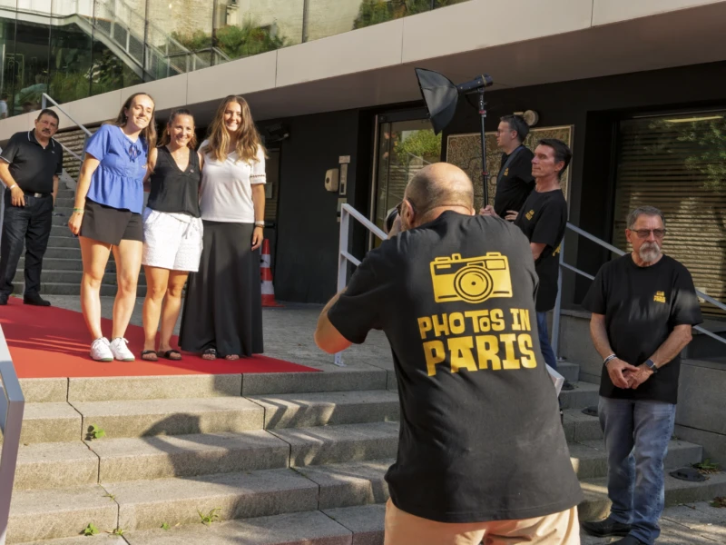 Thierry · 23/06/2026 · 3840 x 2560 Cette photographie capture une scène de tapis rouge avec des personnalités posant pour des photographes. Le sujet principal est un groupe de femmes sur le tapis, encadré par des photographes professionnels, dont l’un porte un t-shirt "Photos in Paris".La composition est dynamique, avec un cadrage serré sur les invités et les photographes. La lumière est naturelle, probablement en plein jour, créant des ombres douces. Les couleurs dominantes sont neutres (noir, gris, blanc) avec des touches de rouge sur le tapis et des vêtements colorés des femmes.L’ambiance est professionnelle et festive, typique d’un événement public ou d’une première.