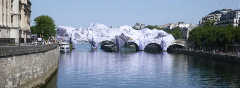 Bao · 5472 x 2005 Cette photographie montre un pont enjambant un cours d’eau, partiellement recouvert de structures blanches et géométriques, évoquant des sculptures ou des installations artistiques.La composition est horizontale, avec une perspective symétrique. Le cadrage inclut une partie des berges et des bâtiments en arrière-plan. La lumière est naturelle et claire, suggérant un jour ensoleillé. Les couleurs dominantes sont les tons bleus du ciel et de l’eau, contrastant avec les blancs des installations et les gris des pierres et bâtiments.Le style est réaliste, avec une ambiance à la fois urbaine et artistique, créant une impression de modernité et de créativité.