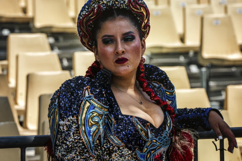 Thierry · 05/07/2026 · 3840 x 2560 Cette photographie met en scène une femme comme sujet principal, vêtue d’un costume opulent et coloré évoquant un style théâtral ou opératique. Le cadrage est serré, centré sur son visage et sa tenue, avec un arrière-plan flou de sièges vides.La lumière semble naturelle et douce, mettant en valeur ses traits et les détails de sa tenue. Les couleurs dominantes sont vives : bleus, rouges, ors et motifs floraux. L’ambiance est dramatique et élégante, renforcée par son expression intense et son attitude théâtrale. Le style rappelle l’opéra ou une représentation artistique.