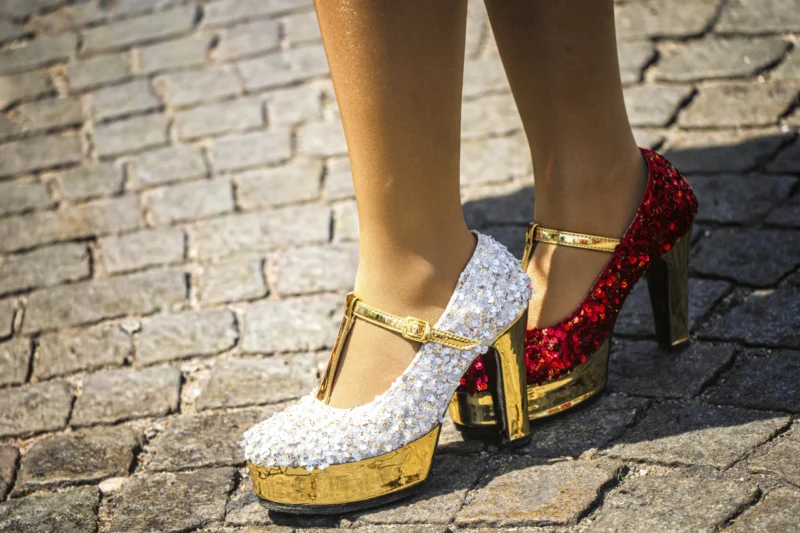 Thierry · 05/07/2026 · 3840 x 2560 Cette photographie met en scène des **chaussures à talons aiguilles** comme sujet principal. La composition est centrée sur les pieds, avec un cadrage serré qui isole les escarpins.Les couleurs dominantes sont le **doré**, le **blanc** (paillettes) et le **rouge** (rubans). La lumière semble naturelle, mettant en valeur les détails des chaussures. Le style est **élégant et festif**, évoquant un mélange de glamour et de sophistication. L’ambiance est **chic et audacieuse**, renforcée par les textures brillantes et les motifs audacieux.