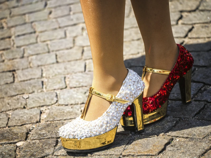 Thierry · 05/07/2026 · 3840 x 2560 Cette photographie met en scène des **chaussures à talons aiguilles** comme sujet principal. La composition est centrée sur les pieds, avec un cadrage serré qui isole les escarpins.Les couleurs dominantes sont le **doré**, le **blanc** (paillettes) et le **rouge** (rubans). La lumière semble naturelle, mettant en valeur les détails des chaussures. Le style est **élégant et festif**, évoquant un mélange de glamour et de sophistication. L’ambiance est **chic et audacieuse**, renforcée par les textures brillantes et les motifs audacieux.