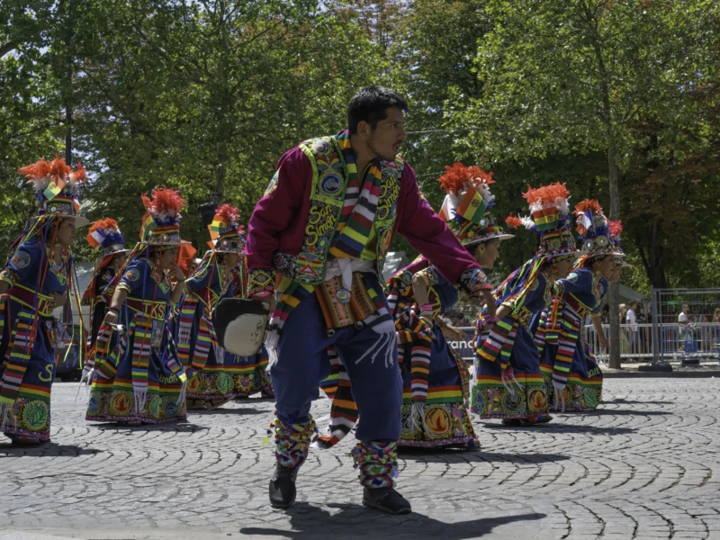 Alice · 05/07/2026 · 6252 x 4168 Cette photographie capture une danse traditionnelle collective. Le sujet principal est un groupe de danseurs vêtus de costumes colorés et ornés de motifs complexes, incluant des coiffures distinctives. La composition montre une formation circulaire, avec un danseur en premier plan, légèrement isolé.Le cadrage est serré, mettant en valeur les détails des costumes et des mouvements. La lumière naturelle, douce et légèrement filtrée, éclaire la scène sans créer d’ombres marquées. Les couleurs dominantes sont vives : rouges, bleus, jaunes et verts, renforçant l’aspect festif.L’ambiance est joyeuse et dynamique, évoquant une célébration culturelle riche.