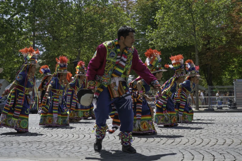 Alice · 05/07/2026 · 6252 x 4168 Cette photographie capture une danse traditionnelle collective. Le sujet principal est un groupe de danseurs vêtus de costumes colorés et ornés de motifs complexes, incluant des coiffures distinctives. La composition montre une formation circulaire, avec un danseur en premier plan, légèrement isolé.Le cadrage est serré, mettant en valeur les détails des costumes et des mouvements. La lumière naturelle, douce et légèrement filtrée, éclaire la scène sans créer d’ombres marquées. Les couleurs dominantes sont vives : rouges, bleus, jaunes et verts, renforçant l’aspect festif.L’ambiance est joyeuse et dynamique, évoquant une célébration culturelle riche.