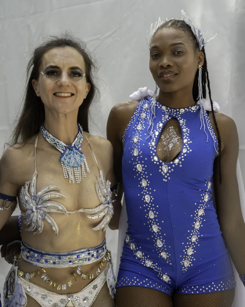 Alice · 05/07/2026 · 4672 x 5840 Cette photographie met en scène deux femmes souriantes, vêtues de costumes exotiques et colorés. Le sujet principal est leur tenue et leur pose joyeuse.La composition montre un cadrage serré sur elles, en pied. La lumière est douce et uniforme, éclairant bien leurs visages et leurs costumes. Les couleurs dominantes sont le bleu électrique, l’or et le blanc, avec des détails argentés.Le style évoque un mélange de folklore et de spectacle, évoquant une ambiance festive et théâtrale, probablement liée à une danse ou un défilé.