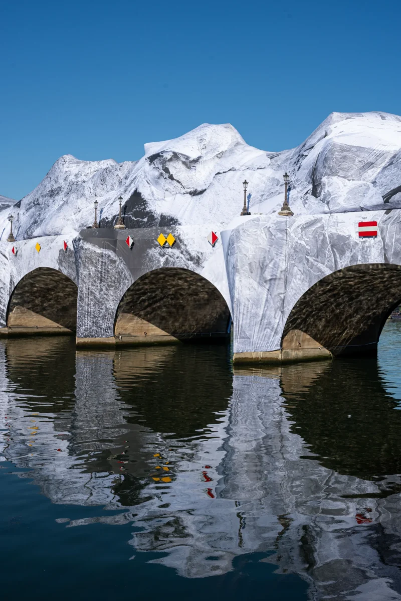 Jean-Marc · 27/05/2026 · 5857 x 3905 Cette photographie met en scène des **blocs de glace géants** sculptés en forme d’arcs, reposant sur l’eau. Le **sujet principal** est ces structures glacées, reflétées dans une surface d’eau calme.La **composition** est symétrique, avec un **cadrage serré** centré sur les arcs. La **lumière**, naturelle et vive, accentue les contrastes et les textures glacées. Les **couleurs dominantes** sont le blanc éclatant de la glace, le bleu du ciel et l’eau, ainsi que des touches de gris et de noir.Le **style** est épuré et artistique, évoquant une ambiance **minérale et presque surréaliste**, mêlant nature et intervention humaine.