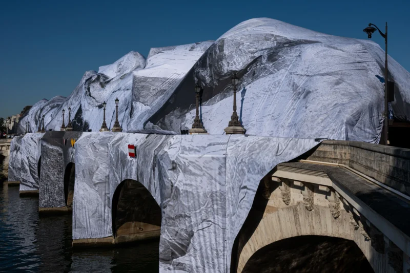 Jean-Marc · 27/05/2026 · 5641 x 3761 Cette photographie montre un pont recouvert de sculptures géantes en forme de blocs de glace ou de montagnes, enveloppées dans un tissu blanc. Le sujet principal est cette installation artistique spectaculaire.La composition met en valeur les structures architecturales du pont, avec une perspective légèrement en contre-plongée. Le cadrage inclut une partie de l’eau en bas et un ciel dégagé en haut.La lumière est naturelle, probablement en journée, créant des contrastes nets. Les couleurs dominantes sont le blanc des sculptures et le gris des structures du pont, renforçant une ambiance froide et mystérieuse. Le style évoque une œuvre contemporaine artistique, immersive et poétique.