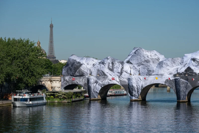 Jean-Marc · 27/05/2026 · 5742 x 3828 Cette photographie montre le pont des Arts à Paris enveloppé de protections métalliques en forme de cylindres, souvent appelées "bulles" pour préserver la structure. Le sujet principal est ce pont recouvert, avec en arrière-plan la Tour Eiffel.La composition met en valeur la symétrie et la répétition des éléments. Le cadrage est large, incluant une partie de la Seine et un bateau. La lumière est naturelle et douce, créant des contrastes subtils. Les couleurs dominantes sont les tons gris des bulles, le bleu de l’eau et le vert des arbres. L’ambiance est à la fois artistique et urbaine, évoquant une touche de créativité dans un cadre parisien emblématique.