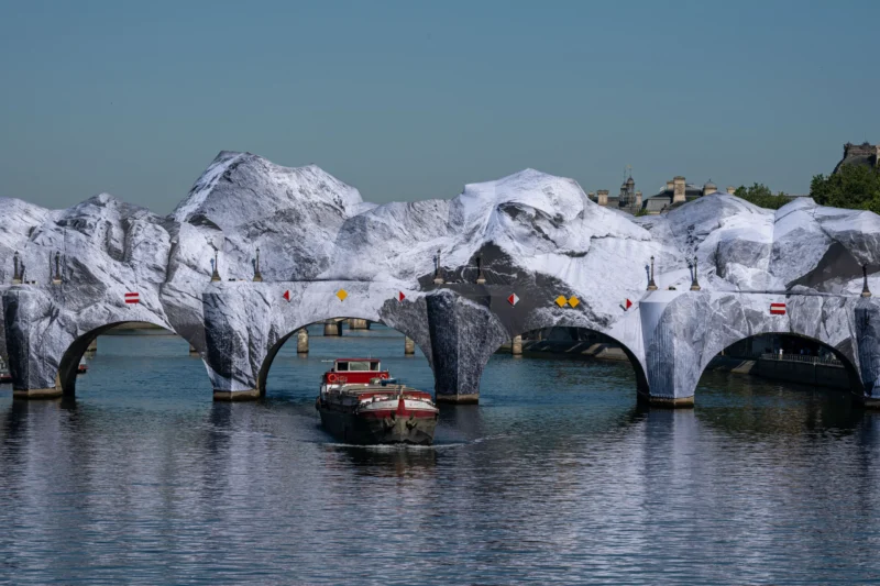 Jean-Marc · 27/05/2026 · 5481 x 3654 Cette photographie montre un bateau rouge naviguant sous une structure architecturale futuriste recouverte de glace ou de structures blanches géométriques. Le sujet principal est le contraste entre le bateau et les arches glacées.La composition est dynamique, avec un cadrage serré sur le bateau et les arches en arrière-plan. La lumière semble naturelle, avec des tons doux et une ambiance légèrement brumeuse. Les couleurs dominantes sont les blancs des structures, le rouge du bateau et les bleus grisâtres de l’eau. Le style évoque une ambiance onirique et artistique, mêlant nature et architecture.