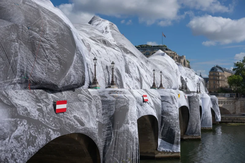 Jean-Marc · 01/07/2026 · 5846 x 3897 Cette photographie montre une série de voitures recouvertes de tissu blanc, alignées sur une berge. Le sujet principal est ces véhicules enveloppés, évoquant une installation artistique ou un événement temporaire.La composition est symétrique et linéaire, avec un cadrage serré sur les voitures et un arrière-plan de bâtiments et d’eau. La lumière est naturelle, avec un ciel dégagé apportant une ambiance claire et lumineuse. Les couleurs dominantes sont le blanc des tissus et les teintes bleutées du ciel et de l’eau.Le style est épuré et contemporain, créant une ambiance à la fois mystérieuse et esthétique.