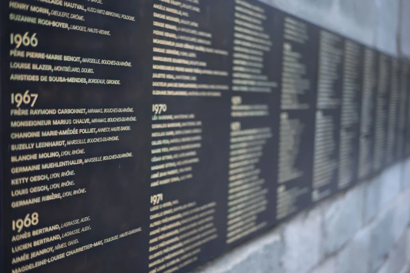 Jean-Marc · 01/07/2026 · 6048 x 4032 Cette photographie montre un mur commémoratif listant des noms et des dates (1966, 1967, 1968). Le sujet principal est les inscriptions gravées, probablement en hommage à des victimes ou événements historiques.La composition est verticale, avec un cadrage serré sur les plaques noires. La lumière naturelle éclaire uniformément la surface, créant des contrastes nets entre le texte blanc et le fond sombre. Les couleurs dominantes sont le noir et le blanc, renforçant une ambiance sobre et solennelle. Le style épuré et minimaliste évoque la mémoire et la gravité.
