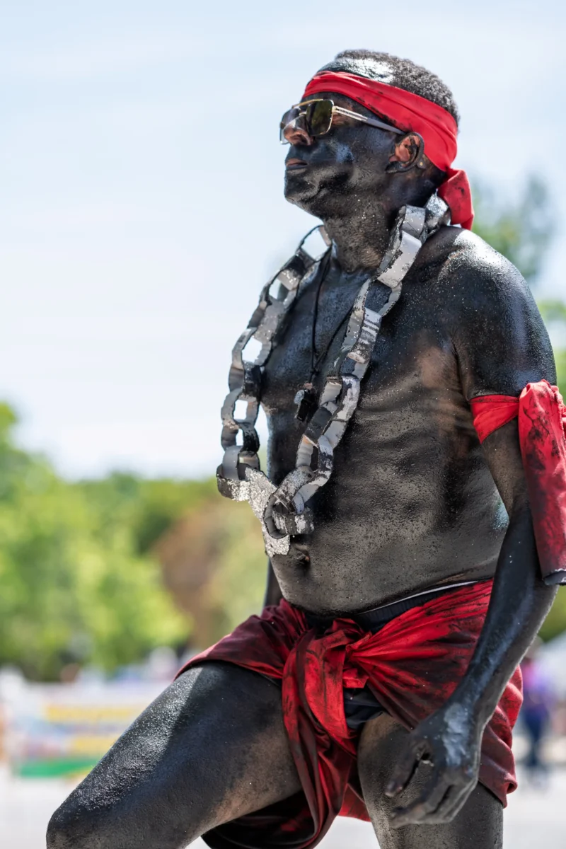 Daniel · 05/07/2026 · 3933 x 5900 Cette photographie met en scène un homme peint en noir, vêtu de parures traditionnelles rouges et blanches. Il semble poser avec une posture confiante, un pied surélevé.Le cadrage est serré, centré sur son visage et son torse, isolant le sujet. La lumière naturelle éclaire son visage, créant des contrastes nets. Les couleurs dominantes sont le noir (peinture corporelle), le rouge (vêtements et accessoires) et le blanc (collier et bandeau).L’ambiance évoque une célébration culturelle ou une cérémonie traditionnelle, avec un style authentique et solennel.