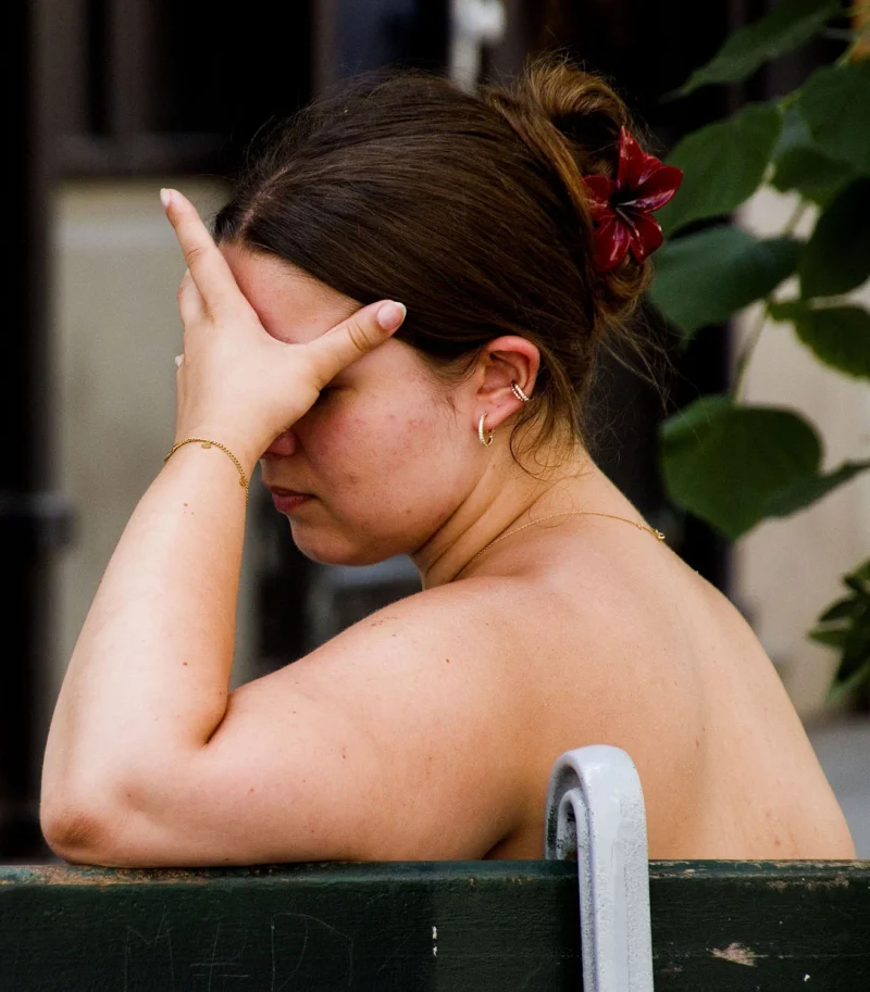 Pascale CHESNOT · 30/05/2026 · 1314 x 1500 Une personne au bain public, les yeux couverts d'une main, avec une fleur rouge dans les cheveux et des boucles d’oreilles