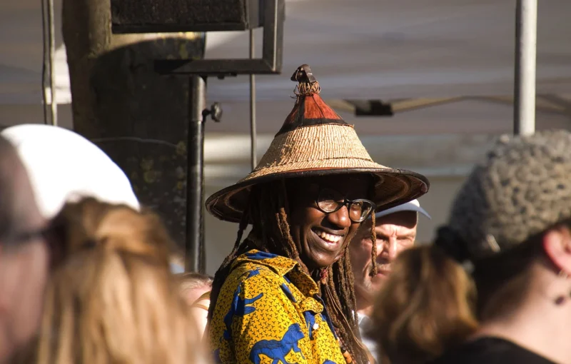 Pascale · 12/07/2026 · 1500 x 956 Personne souriante portant un chapeau traditionnel en paille et des lunettes, entourée d’un groupe en extérieur.