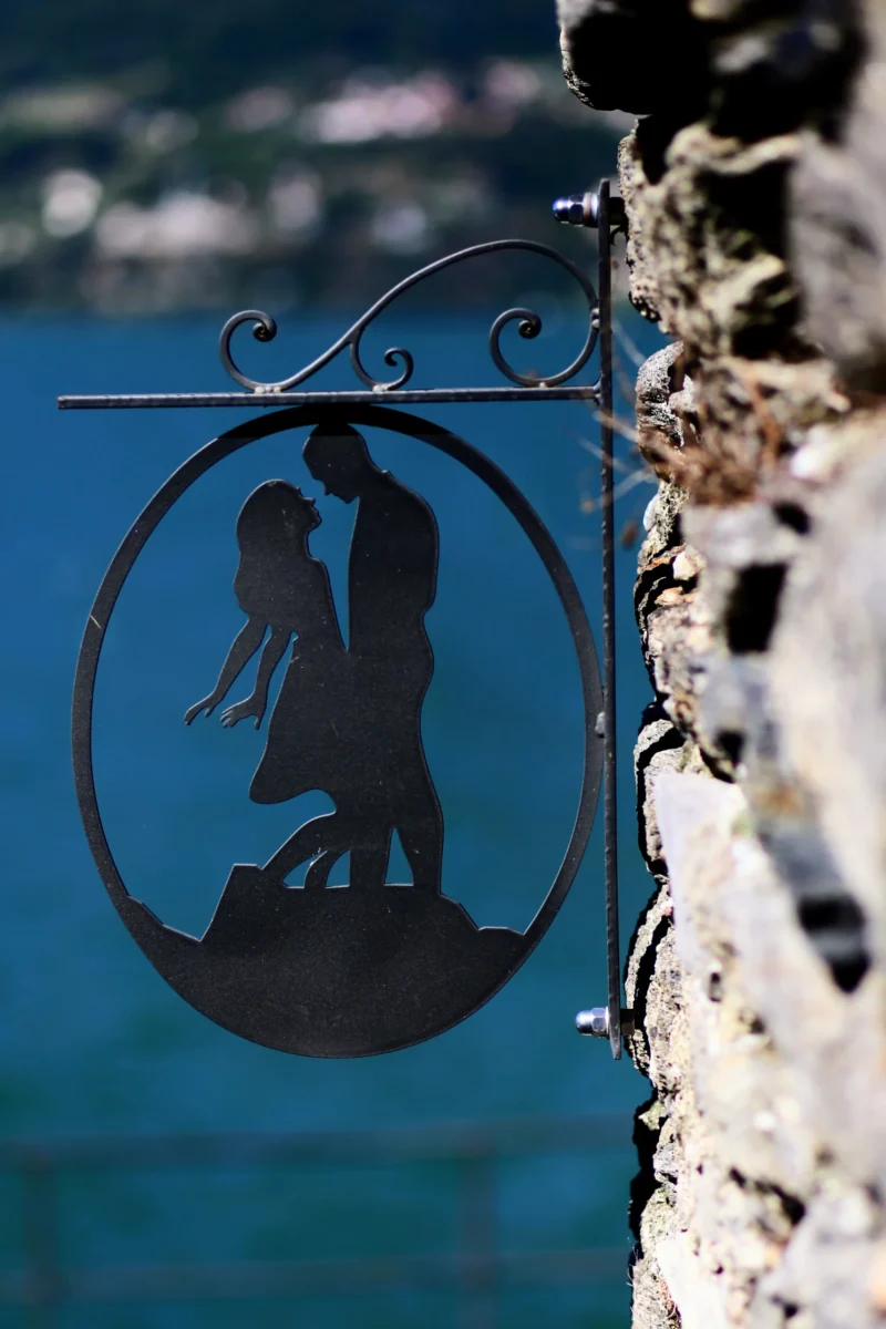 Fabienne · 22/08/2026 · 3017 x 4525 Sculpture métallique représentant deux silhouettes en position de danse ou d'étreinte sur fond d'eau bleue, fixée à