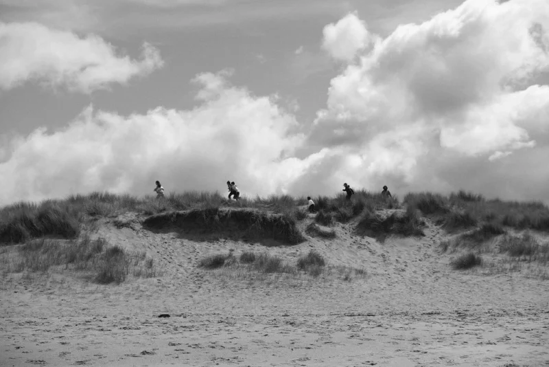 Léonard · 1024 x 683 Quatre silhouettes en mouvement sur une dune de sable avec un ciel nuageux en arrière-plan, ambiance dynamique et naturelle.