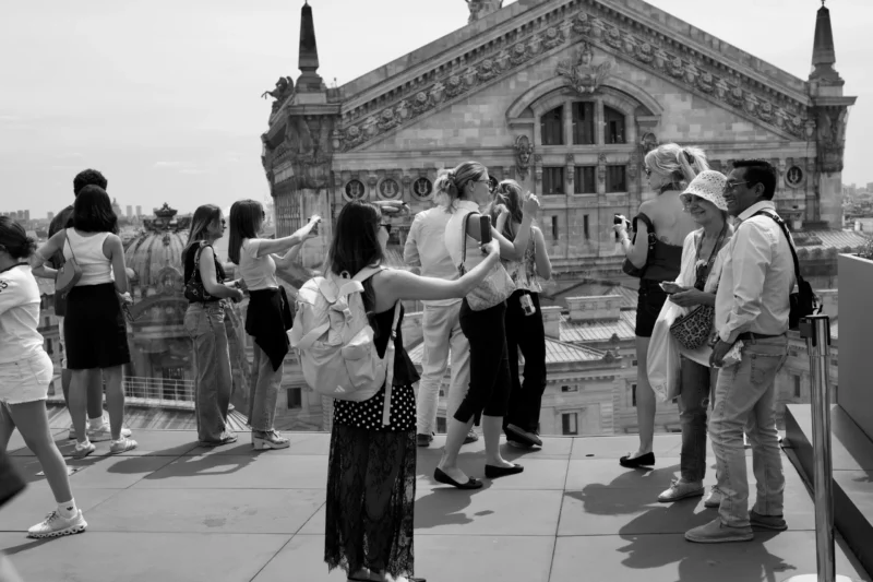 Jean Claude · 19/07/2026 · 5524 x 3682 Groupe de personnes sur une terrasse observant un bâtiment historique en ville, en noir et blanc, ambiance touristique