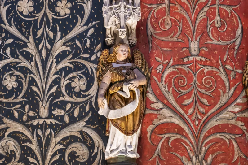Daniel · 23/07/2026 · 4017 x 2678 Statue religieuse centrale entourée de motifs décoratifs dorés sur fond bleu et rouge, style baroque ornemental.