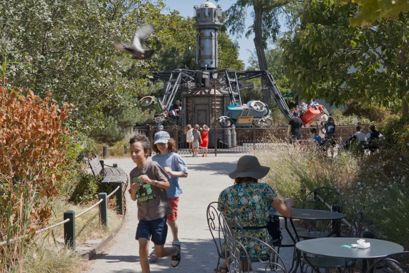 Frédéric · 07/08/2026 · 2517 x 1680 Deux enfants marchent vers une attraction touristique en plein air avec une structure métallique et des véhicules suspendus