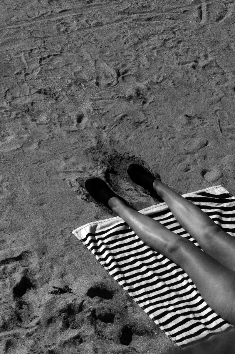 Thomas · 28/07/2026 · 1769 x 2660 Pieds en sandales à rayures noires et blanches posés sur du sable avec des traces autour, vue aérienne.