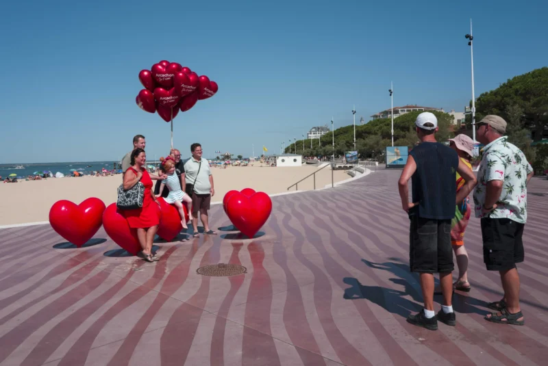 Jean-Philippe · 21/07/2026 · 3840 x 2569 Groupe de personnes sur une promenade en bois près d’une plage, entourées de ballons en forme de cœurs rouges et d’un