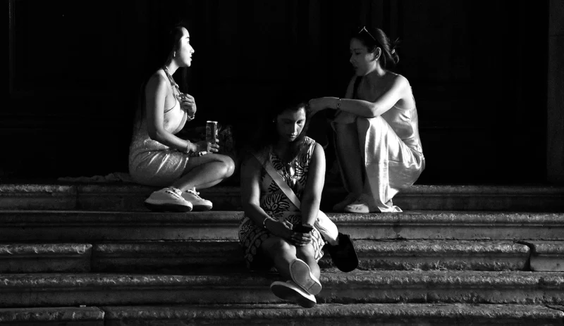 Franck T. · 09/07/2026 · 1400 x 811 Trois personnes assises sur des marches, l’une tient un verre, les autres semblent discuter dans une ambiance nocturne