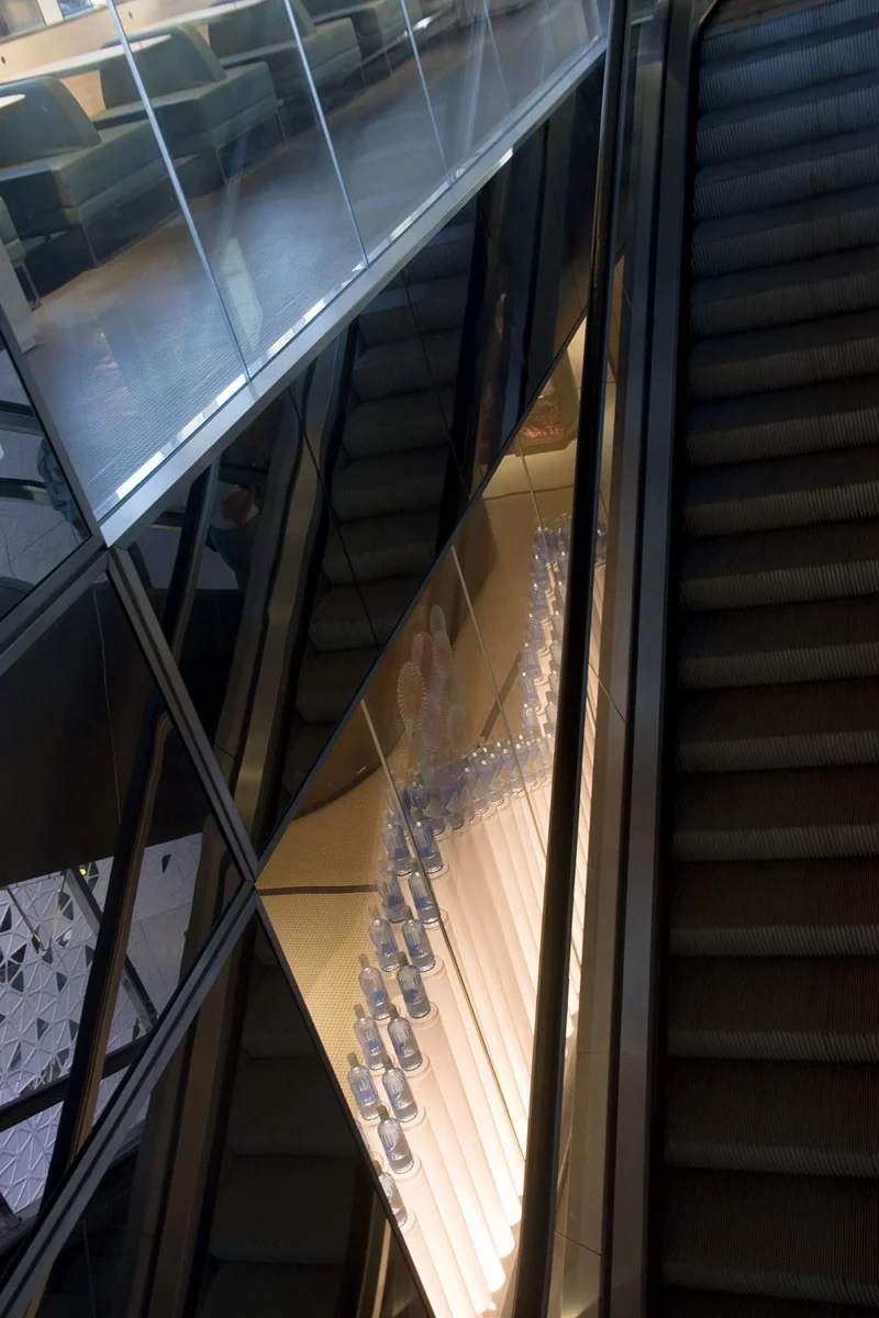 Escalier mécanique dans un bâtiment moderne avec une rampe de lumière bleutée et des structures géométriques en verre